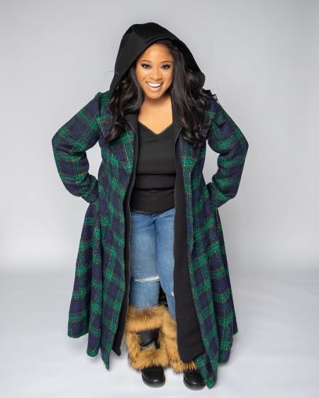 Kierra Sheard in a black top and green over coat poses for a picture.